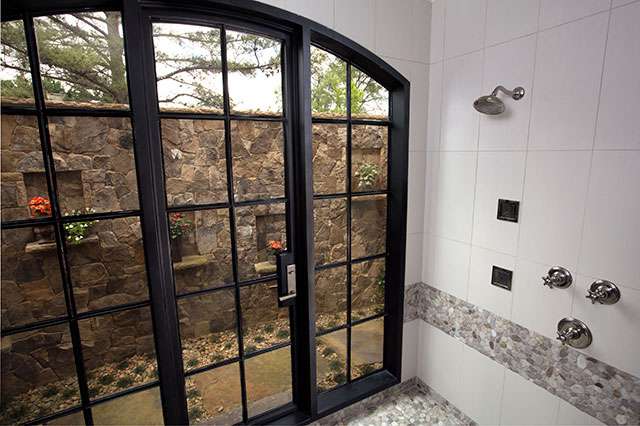 glass doors from outside leading into shower looking at stone wall with trees behind it