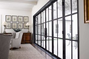 steel glass doors with black trim gallery wall over dresser in living room with rug and grey chairs